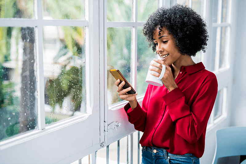 woman-standing-near-window-looking-at-cell-phone